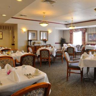 A formal dining room with neatly arranged tables and chairs, each covered with white tablecloths.