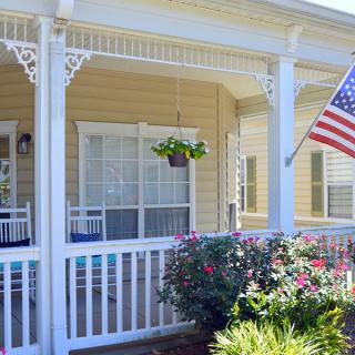 A charming porch adorned with a hanging plant and an American flag, surrounded by vibrant flowers.
