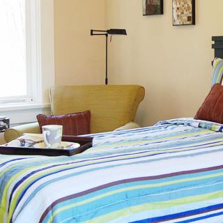 A cozy bedroom with striped bedding and a tray on the bed.