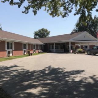 A single-story residential building with a driveway and surrounding trees casting shadows.