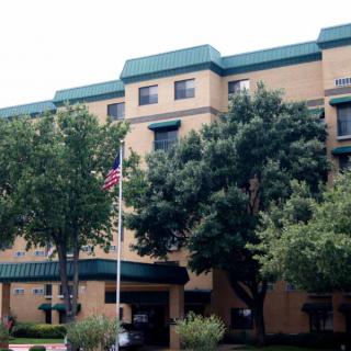 A multi-story building with green accents, surrounded by trees and featuring a flagpole in front.