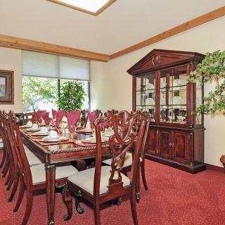 An elegant dining room with a large wooden table, ornate chairs, and a glass-fronted cabinet.