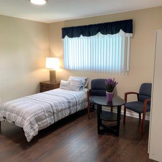 A cozy bedroom with a single bed, two armchairs, and a small table under a window with blue curtains.