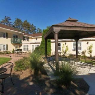 A sunny day in a garden with a gazebo, surrounded by trees and a multi-story building.
