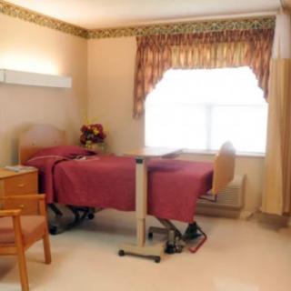 A hospital room featuring a bed, wooden furniture, and a window with curtains.