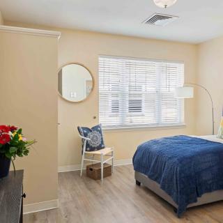 A modern bedroom with a blue bedspread, wooden floor, and decorative elements like a mirror and flowers.