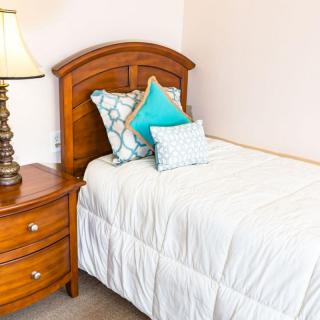 A cozy bedroom with a neatly made bed, colorful pillows, and a wooden nightstand with a lamp.