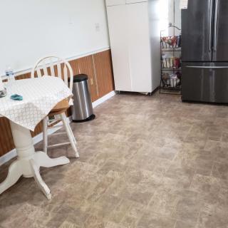 A neat kitchen area featuring a table, chair, stainless steel refrigerator, and trash can.