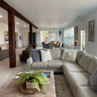 A modern open-space living room with a large sofa, wooden beams, and plenty of natural light.
