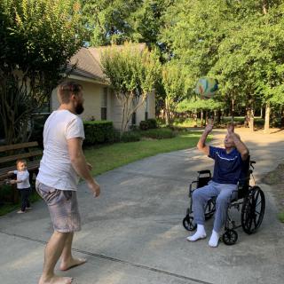 A family enjoying a moment together outdoors, with a person in a wheelchair interacting with others on a sunny day.