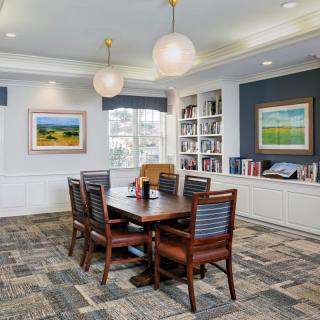 A well-furnished library or conference room featuring a table with chairs, bookshelves, and artwork on the walls.