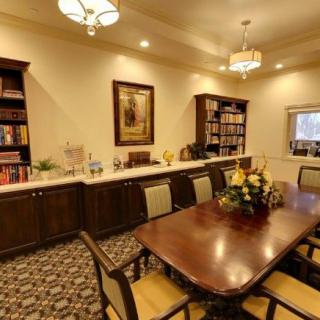 A cozy meeting room with a polished wooden table surrounded by chairs, flanked by bookshelves and adorned with elegant lighting.