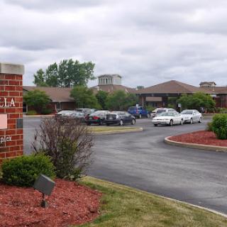 A view of a building surrounded by a parking lot and landscaped areas under a cloudy sky.