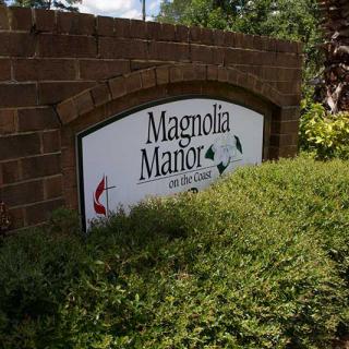 Sign for Magnolia Manor on a brick wall surrounded by greenery.