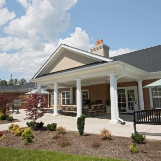 A modern building with a large porch and well-maintained garden under a partly cloudy sky.