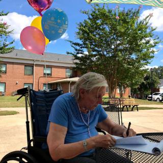 An elderly person enjoying a sunny day outdoors while writing, accompanied by festive balloons.