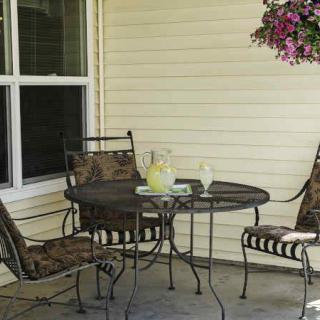 A cozy patio setup with a round table, comfortable chairs, and a pitcher of lemonade next to hanging flowers.
