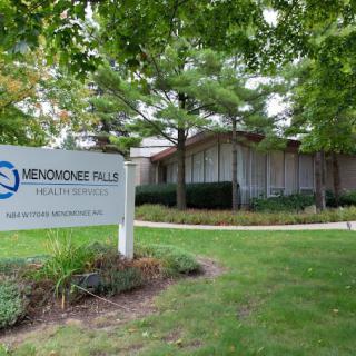 A modern building surrounded by trees and a sign in front on a well-kept lawn.