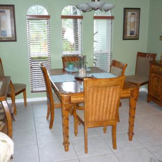 A cozy dining room with a wooden table and chairs, decorated with art pieces and natural light from the windows.
