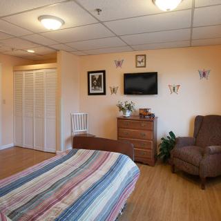 A cozy bedroom with a bed, armchair, dresser, and mounted television.
