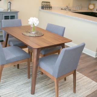 A modern dining area featuring a wooden table surrounded by gray upholstered chairs, set atop a striped rug.