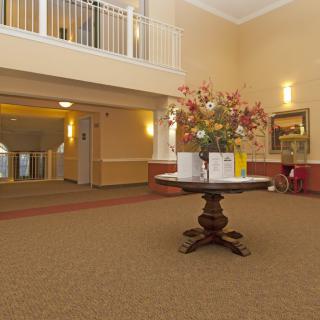 A spacious lobby area with a central table decorated with flowers, under warm lighting and surrounded by hallways.