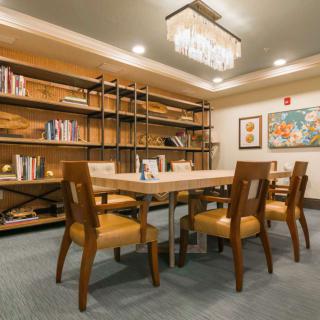 A cozy library setting with a wooden table, chairs, bookshelves, and artwork on the walls.