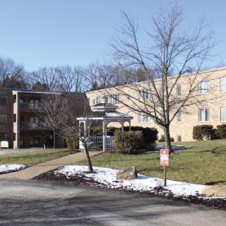 A residential apartment building surrounded by trees with patches of snow on the ground.