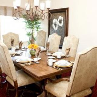 A beautifully arranged dining room with an elegant table setting, featuring a wooden table, upholstered chairs, and a chandelier.