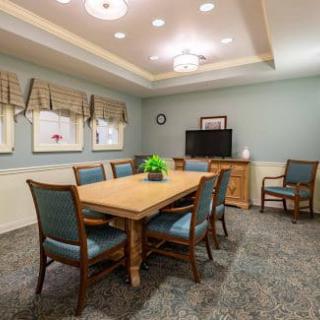 A neatly arranged dining or meeting room with a wooden table, surrounded by upholstered chairs and soft lighting.