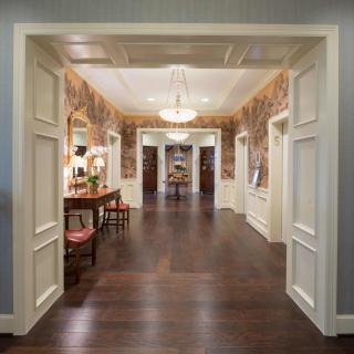 A beautifully decorated hallway with hardwood flooring, elegant wallpaper, and a chandelier.