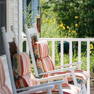 A cozy porch with striped cushioned rocking chairs overlooking a garden.