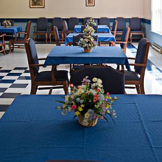 A neatly arranged dining room with blue tablecloths and floral centerpieces.