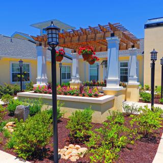 A beautifully landscaped garden featuring a pergola with hanging flowers and ornate lamp posts.