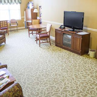 A well-lit living room with a television, chairs, and a table on a carpeted floor.