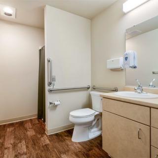 A clean, handicap-accessible bathroom with a toilet, sink, and mirror.