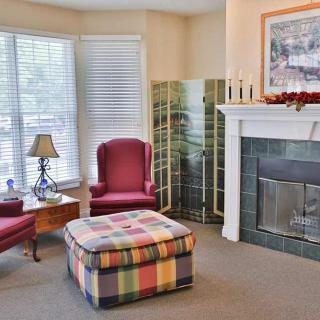A cozy living room featuring a fireplace, red chairs, and a colorful ottoman.