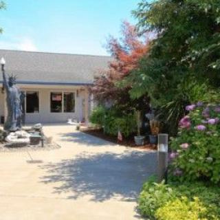 A charming house with a well-maintained garden and patio area surrounded by trees and colorful flowers.