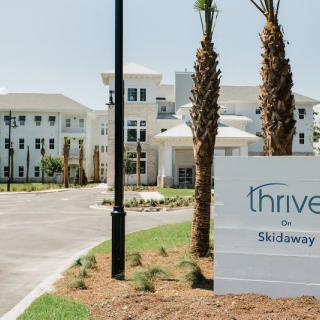 Entrance to a residential building with palm trees and a 'Thrive on Skidaway' sign.