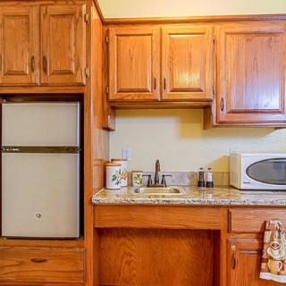 A kitchen with wooden cabinets, featuring a refrigerator, microwave, sink, and countertop.