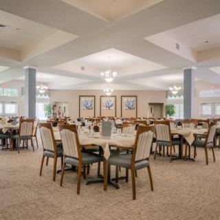 An elegant dining room with multiple tables and chairs, softly lit by chandeliers.