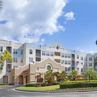 A modern residential building with palm trees and a landscaped entrance under a bright blue sky.