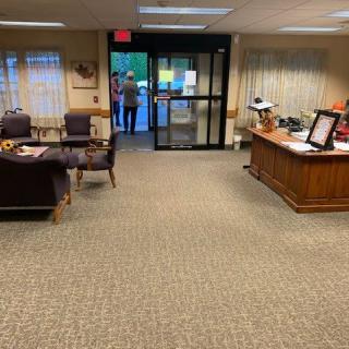 A spacious office reception area with a desk and chairs, featuring a carpeted floor.