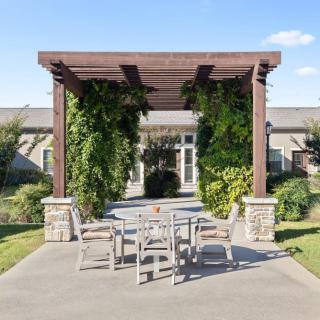 An outdoor patio area featuring a wooden pergola adorned with lush greenery, shading a set of patio furniture on a sunny day.