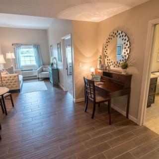 A cozy living space with a desk and mirror, featuring warm lighting and wooden flooring.