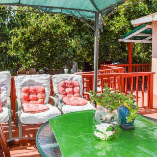 A cozy outdoor patio with cushioned chairs, a green table, and a sunshade, surrounded by lush greenery.