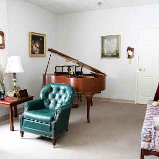 A cozy living room featuring a grand piano and a stylish green chair, adorned with artistic pieces on the walls.