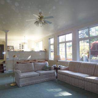 A spacious living room with large windows, a ceiling fan, and comfortable sofas.