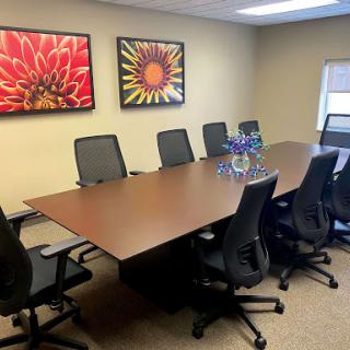 A modern conference room featuring a large wooden table surrounded by ergonomic chairs, complemented by vibrant floral artwork on the walls.