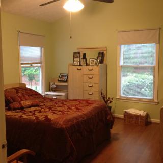 A cozy bedroom with a bed, dresser, and two windows providing natural light.